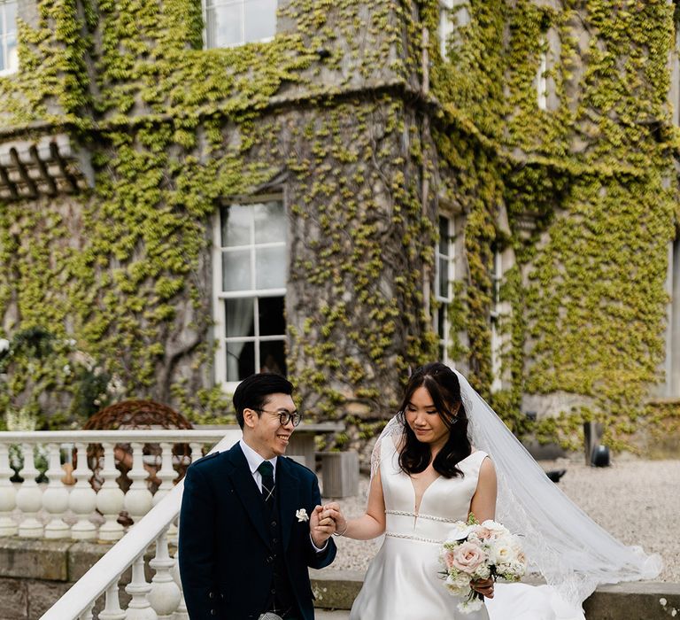 Bride in Princess wedding dress holds her grooms hand who wears tartan kilt