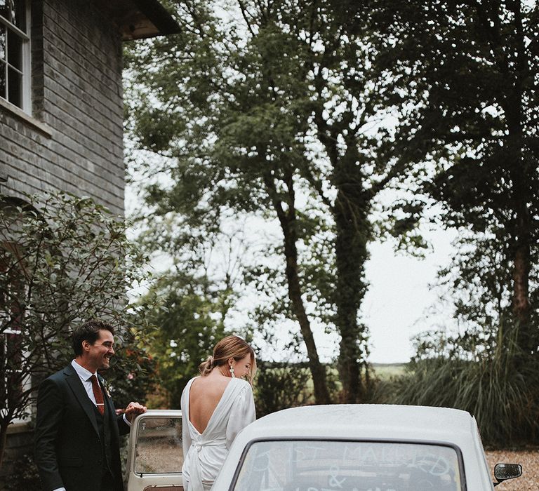 Bride in long sleeve wedding dress & groom get into vintage Fiat 126 wedding car 