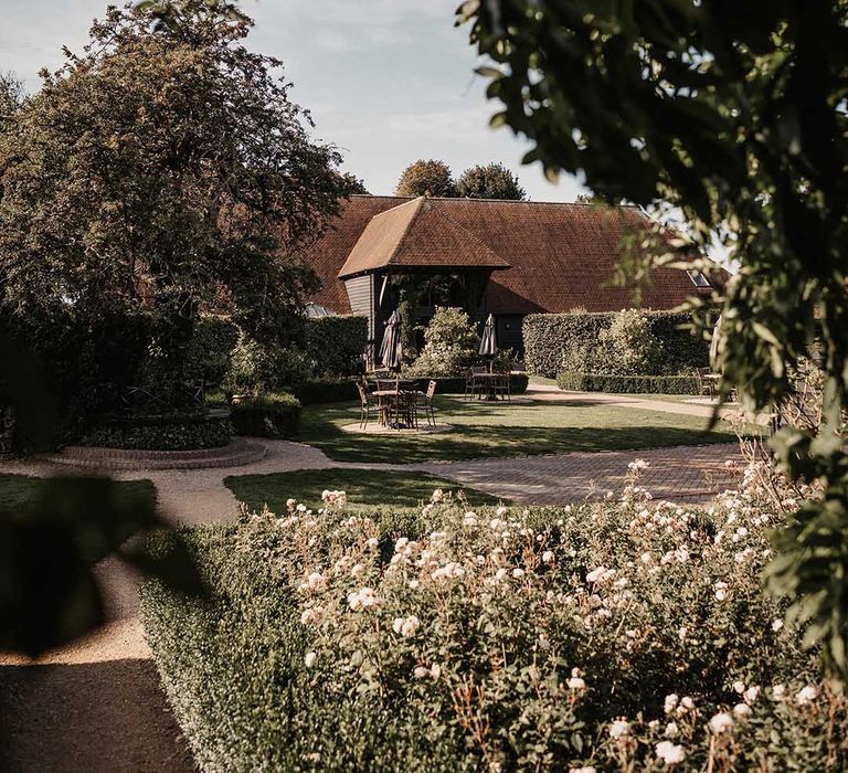 Exterior of The Old Kent Barn wedding venue with flower bushes and outdoor table and chairs 