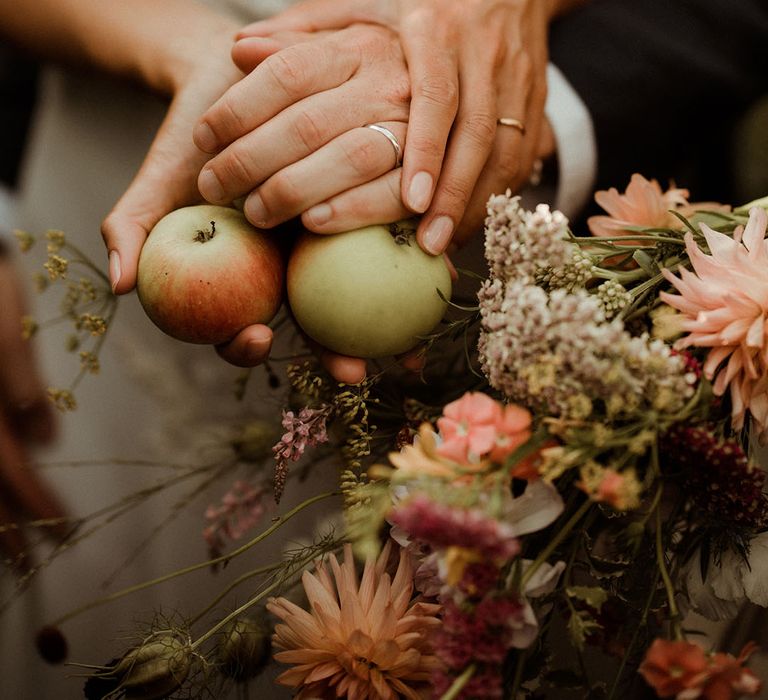 Bride and groom holding apples wearing their gold and silver wedding bands 