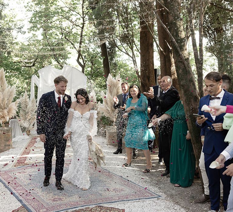 Bride & groom walk through confetti across Moroccan styled rugs 