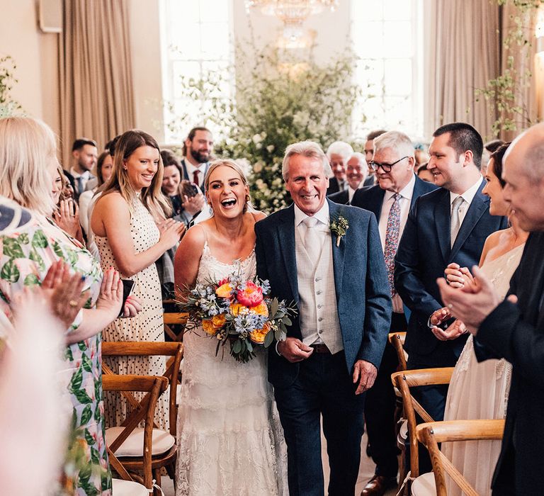 Father of the bride in a three piece suit with a navy jacket and grey tie and waistcoat walks the bride down the aisle for the wedding 