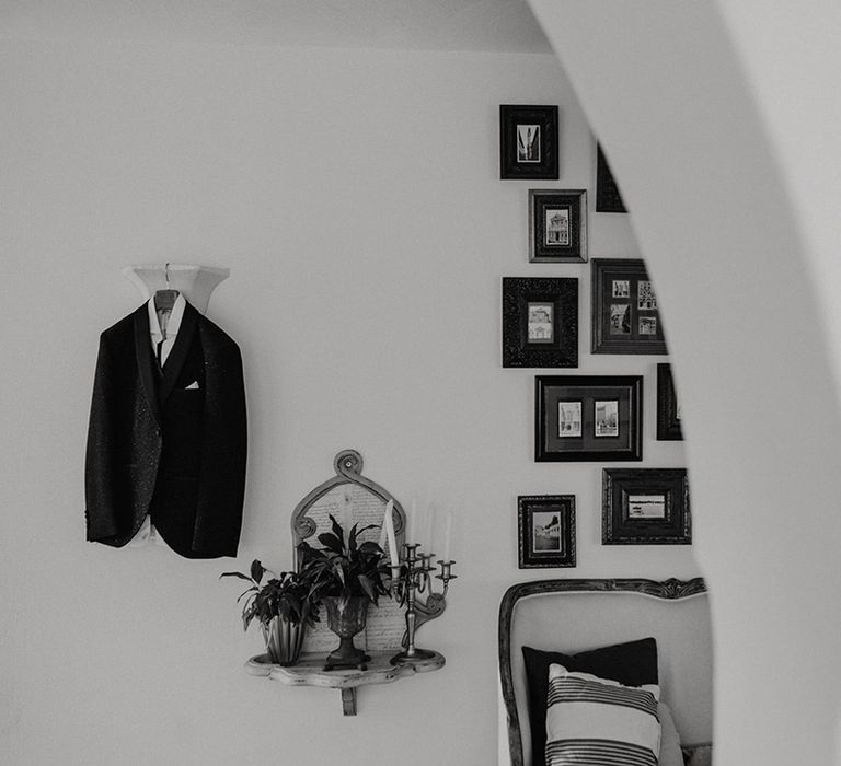 Grooms tuxedo hanging up on the wedding morning next to a gallery wall of pictures 