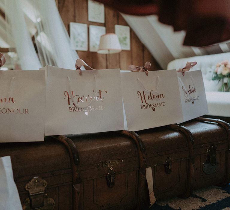 White square shopping bags with pink ribbon and pink metallic font personalised with the bridesmaid's names as wedding presents 