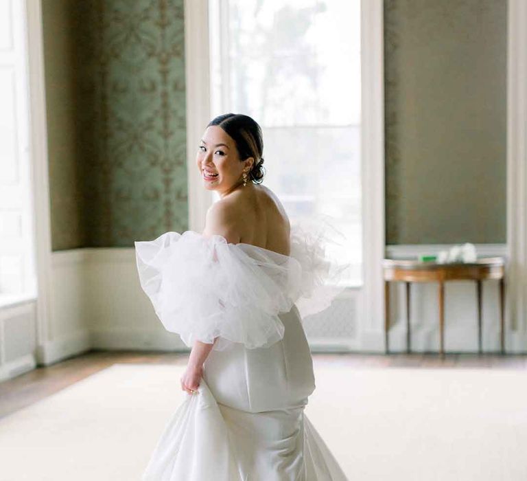 Bride turning and smiling wearing dramatic tulle puff sleeve strapless wedding dress 