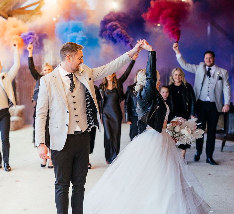 The groom spins the bride around wearing a leather jacket with colourful smoke bombs and the bridesmaids and groomsmen wearing matching black and grey outfits