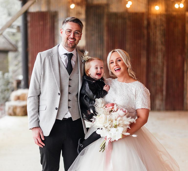 The bride and groom smile with their little girl wearing a black dress and black leather jacket to match the bridal party