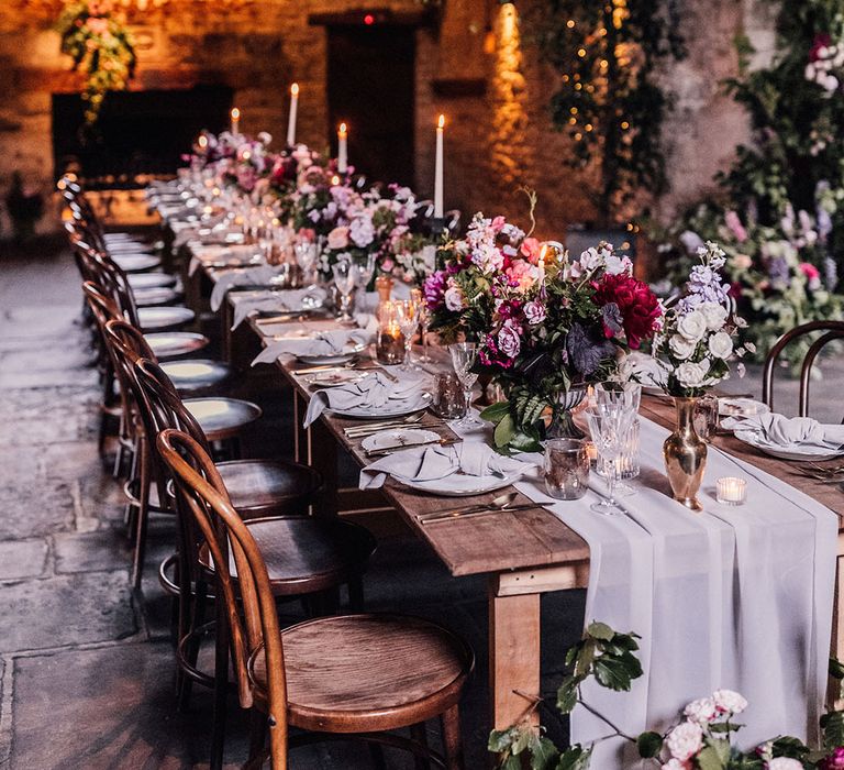 Luxury and intimate wedding at Cripps Barn with a long banquet table covered in candlelight, romantic floral arrangements, and acrylic wedding sign