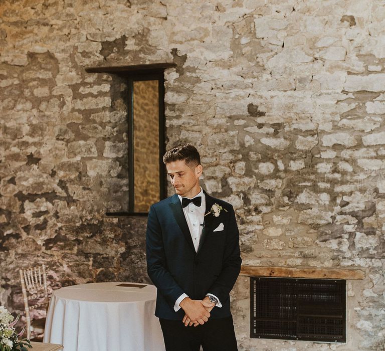 The groom wears a dark blue and black wedding suit for the black tie barn wedding in Bath 