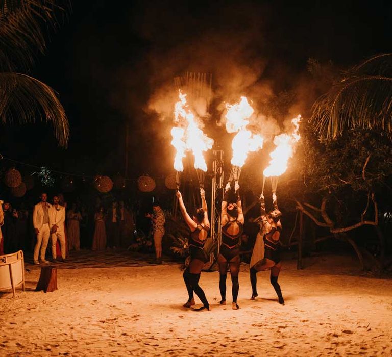 Grooms and wedding guests watching fire dancers at destination LGBTQIA+ wedding in Mexico 