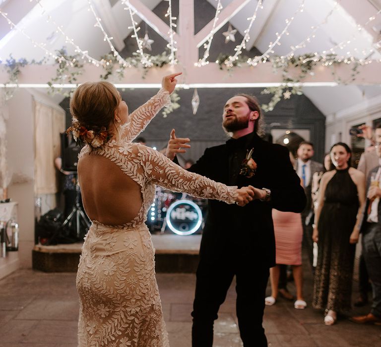 Bride in open back lace wedding dress with long sleeves having her first dance with the groom in a velvet wedding suit 