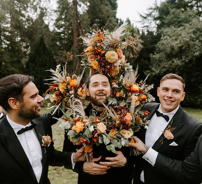 The groomsmen all pose jokingly with the groom surrounded by flowers 