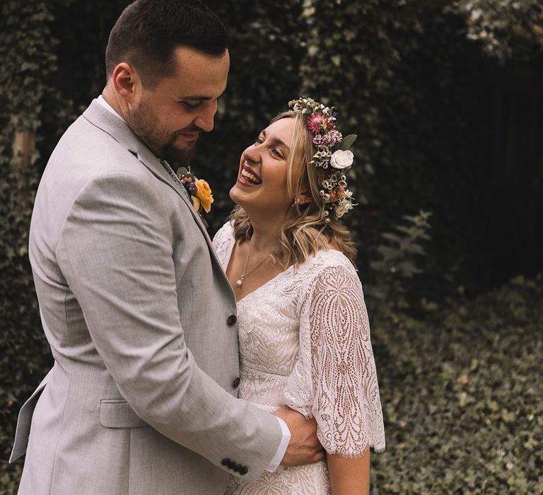 Groom in three piece light grey suit for the wedding day with the bride in lace wedding gown 