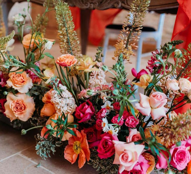 Seasonal wedding flower arrangement with pink and orange garden roses, orange floribunda, yellow ranunculus flowers, foliage and Iceland poppies 