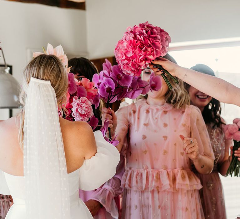 Bride wearing off the shoulder Jesus Peiro wedding dress with off the shoulder puff sleeves with the bridesmaids holding bright pink bouquets 