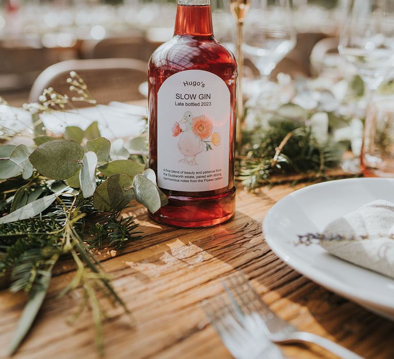 Sloe gin wedding favours made by the groom's family next to foliage table runners and white taper candles in gold candlesticks 