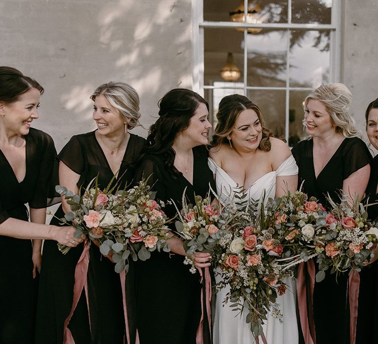 Bridal party wearing black bridesmaid dresses with the bride in an off the shoulder dress holding pink and white bouquets 