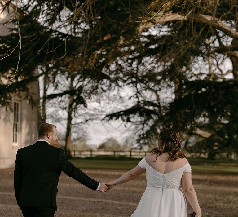 Bride in an off the shoulder Madi Lane wedding dress walking with the groom around the Aswarby Rectory wedding venue 