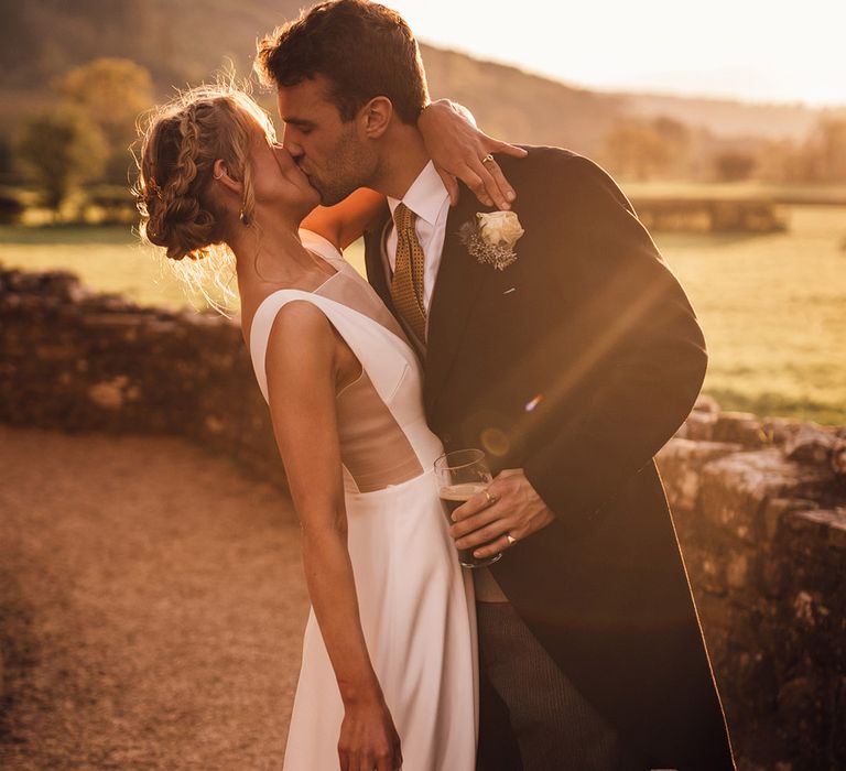 Golden hour sunset wedding photographs with groom in classic morning suit kissing bride in Andrea Hawke gown with mesh insert 