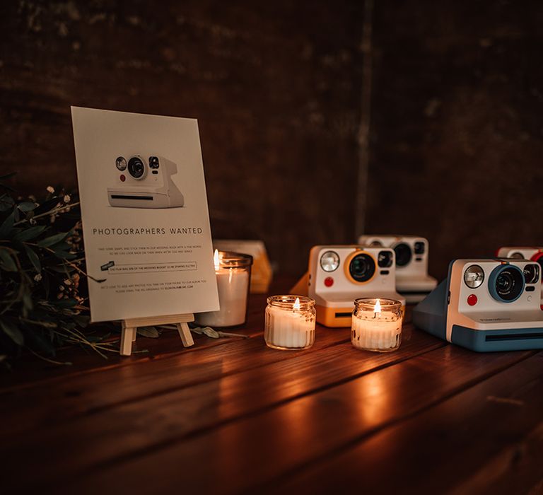 Polaroid cameras on wooden table with sign for guests to snap some memories 