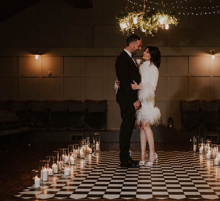 The bride and groom stand on checkerboard dance floor and aisle surrounded by lanterns at Larkspur Lodge wedding 