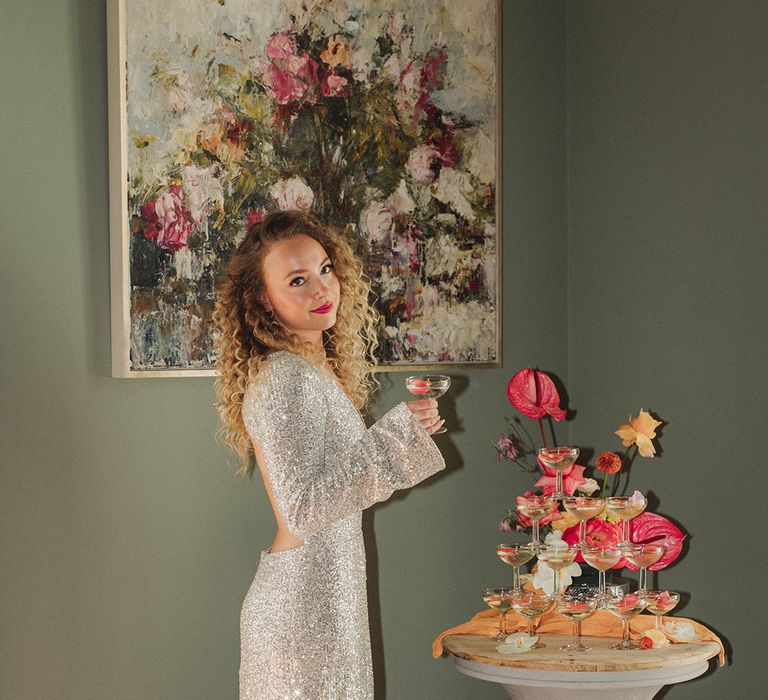 Bride in sparkly silver long sleeve reception dress next to cocktail tower 