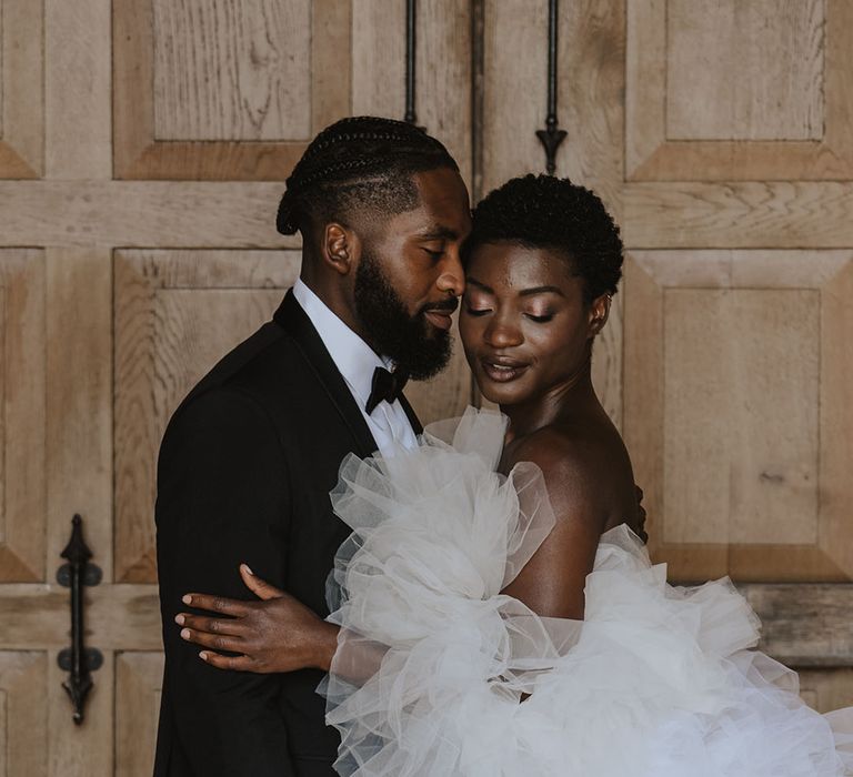 Bride in off the shoulder tulle Millia London wedding dress embracing groom in classic black tie 