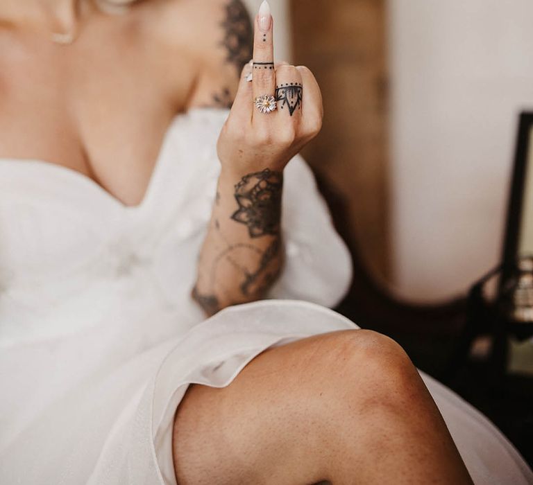 Bride with tattoo wearing a daisy shaped wedding ring with sharp pointed neutral wedding nails 