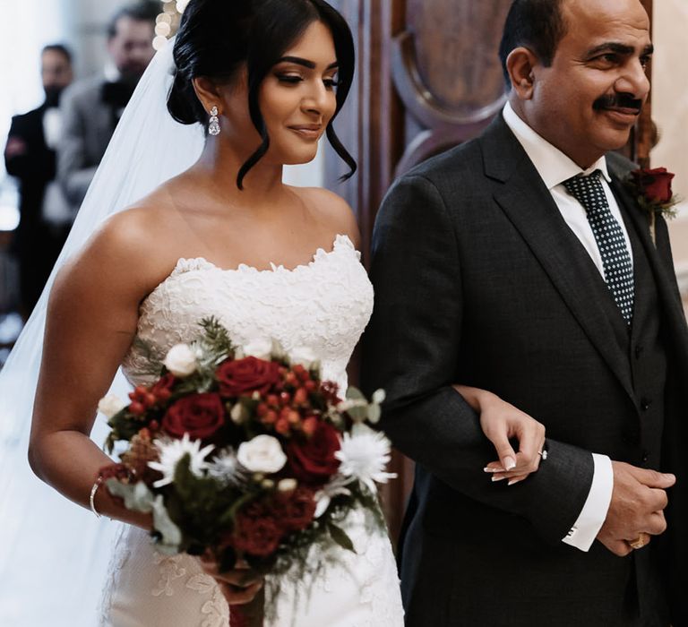 Father of the bride walks the bride down the aisle holding red rose wedding bouquet 