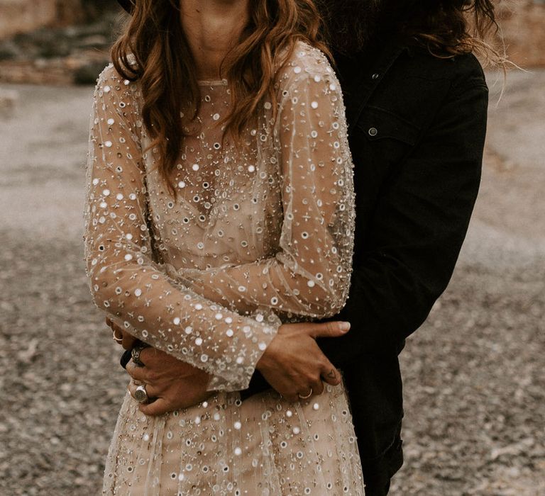 Bride in sparkly gold sequin wedding dress with black hat next to groom in black wedding outfit 