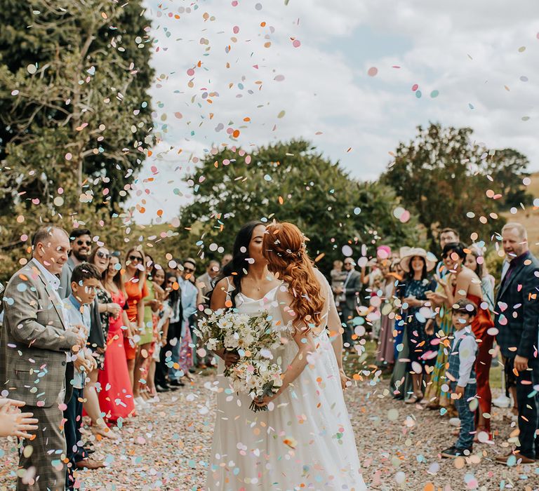 Colourful pastel confetti exit for two brides in white satin wedding dresses 