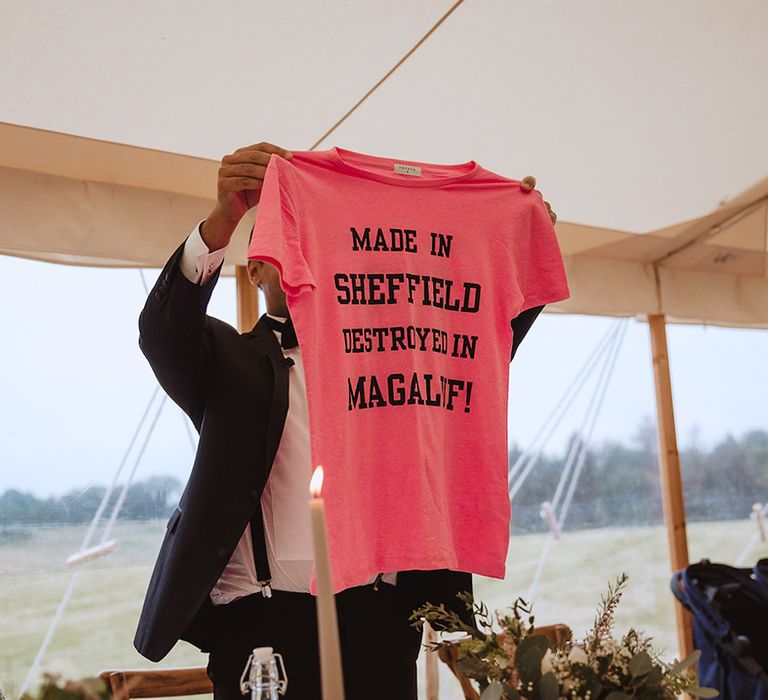 Groom holding up neon pink t shirt with black slogan 