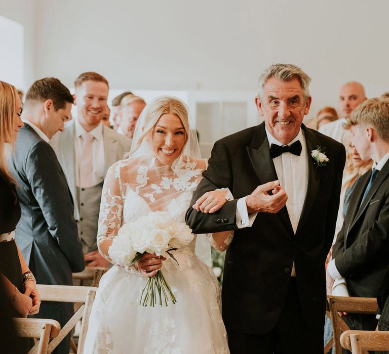 Father of the groom wearing a black tuxedo walking the bride down the aisle 