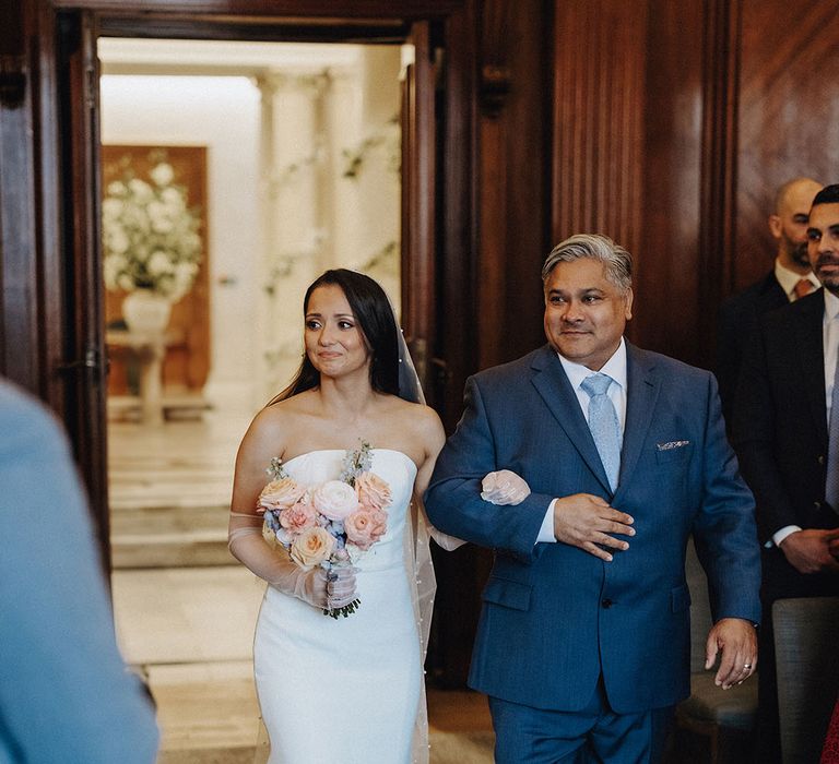 The father of the bride in a blue suit walks the bride down the aisle