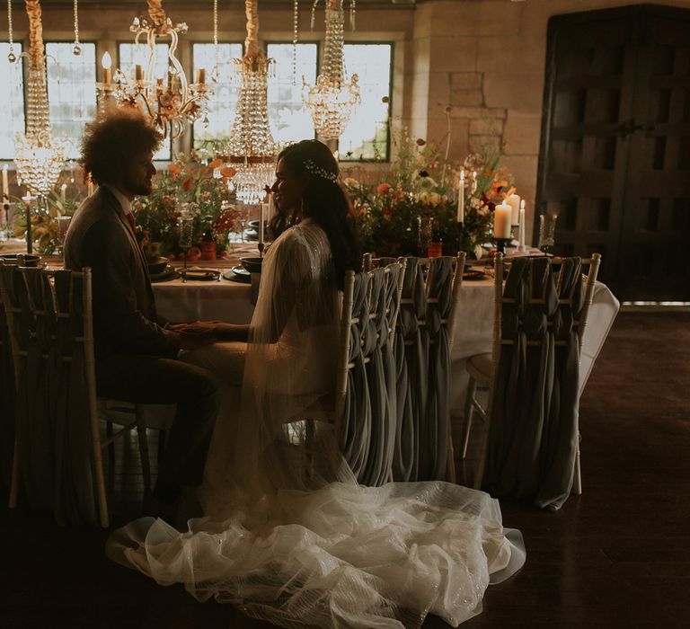 Bride and groom sitting at the intimate wedding reception filled with flowers and light