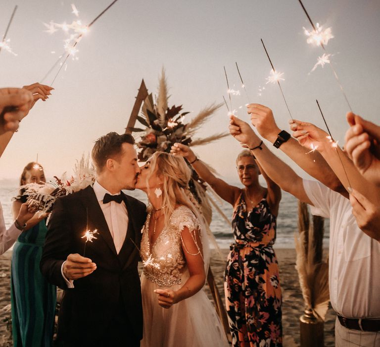 Bride and groom kiss under sparklers at beach wedding