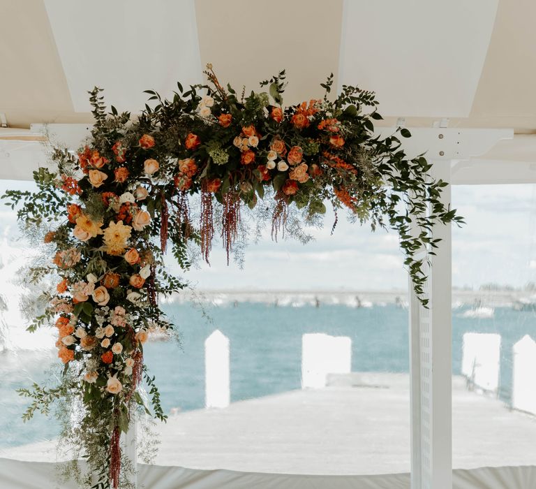 Floral arch altar with peach, orange and coral flowers mixed with green foliage 