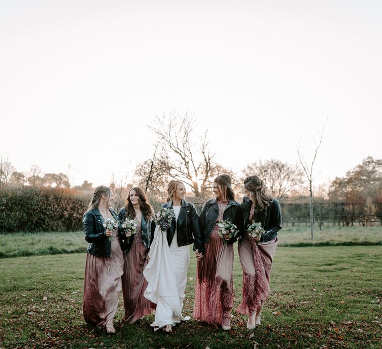 Bridal party portrait with bridesmaids in pink pleated dresses and leather jackets and the bride in a fitted dress with customised leather jacket 