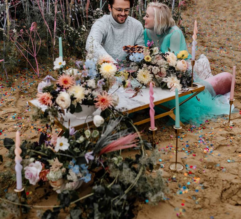 Bride and groom eating pizza on the beach at their intimate elopement with colourful flowers, candles and decor