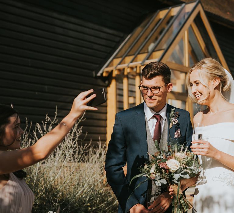 Bride & groom laugh with wedding guests in the sunshine