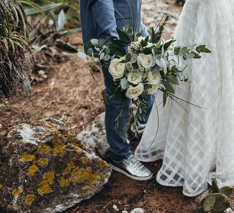 Groom in light blue suit with silver trainers holding a white and green wedding bouquet with eucalyptus and roses 