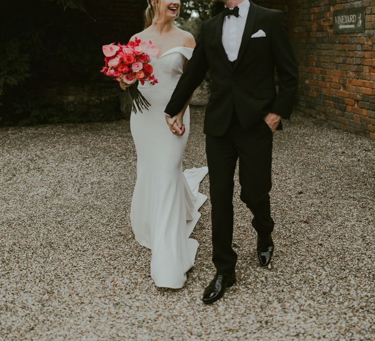 Bride & groom walk through barn grounds whilst holding hands