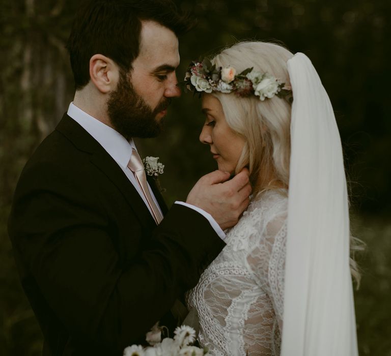 Groom in black Hugo Boss suit holds face of bride in Grace Loves Lace wedding dress and single tier cathedral length veil at Drenagh Estate Wedding