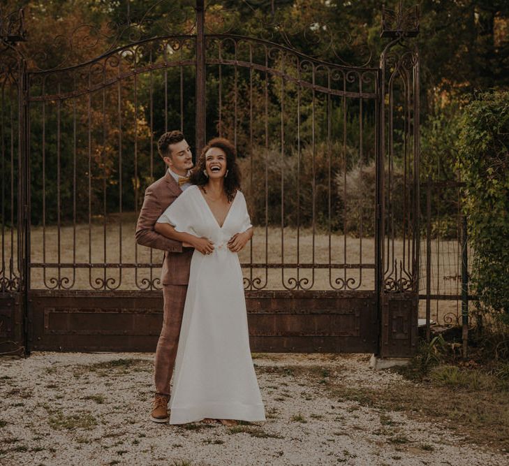 Groom in a brown wedding suit standing behind his bride at the gates of Château de Caumont