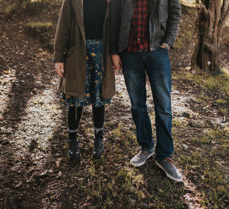 Couple stand together in the forest whilst sun beams through the trees