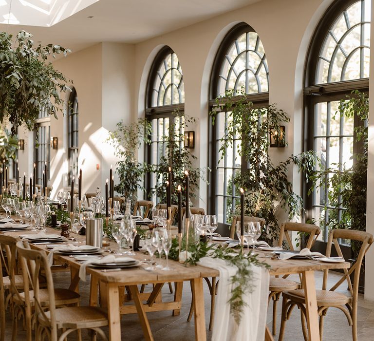 Wooden wedding table with rustic decor, wooden chairs, foliage cloud, greenery and black candles in the Fig House at Middleton Lodge