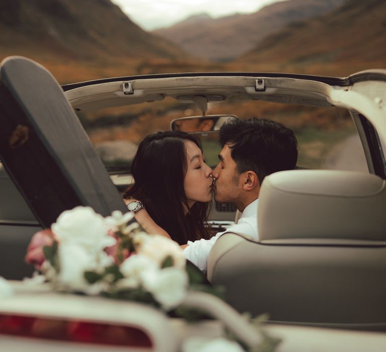 Couple kiss whilst sitting in vintage car