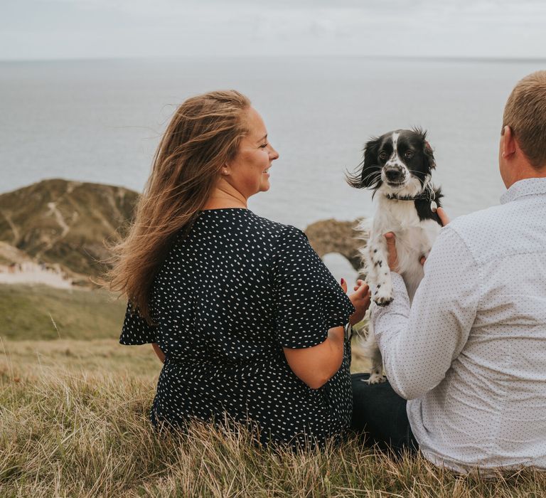 Couple sat over looking Durdle Door with their puppy