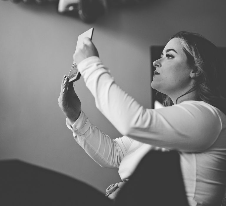 Black & white image of bride looking in mirror after applying makeup