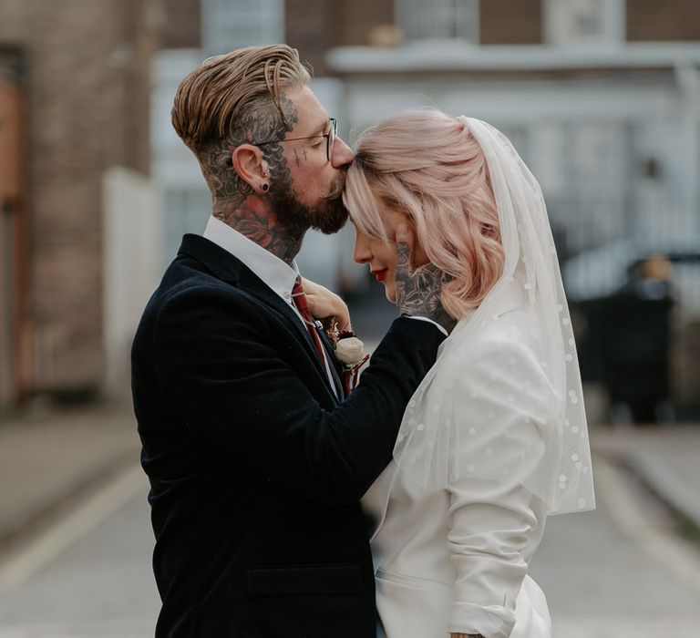 Groom kisses bride on head as she holds bouquet to the side